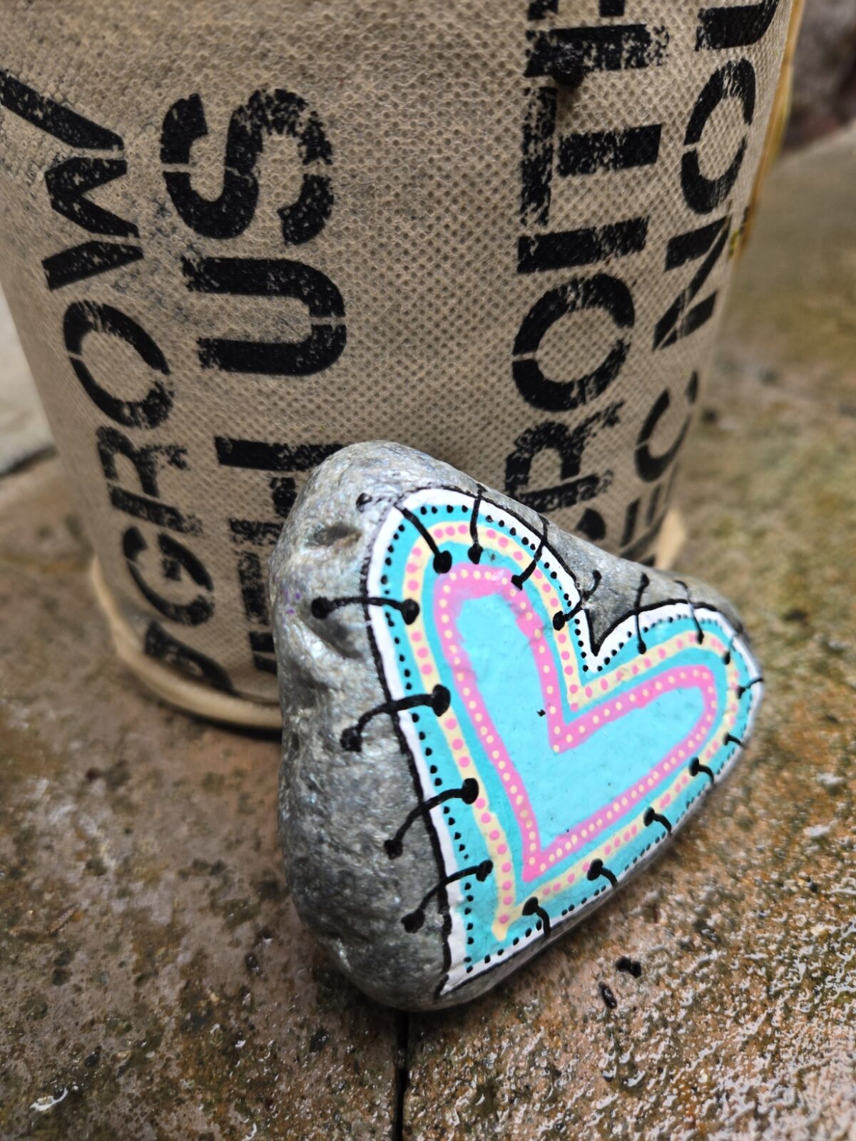 Picture of a painted kindness rock with a stitched heart design in pastel colors. 